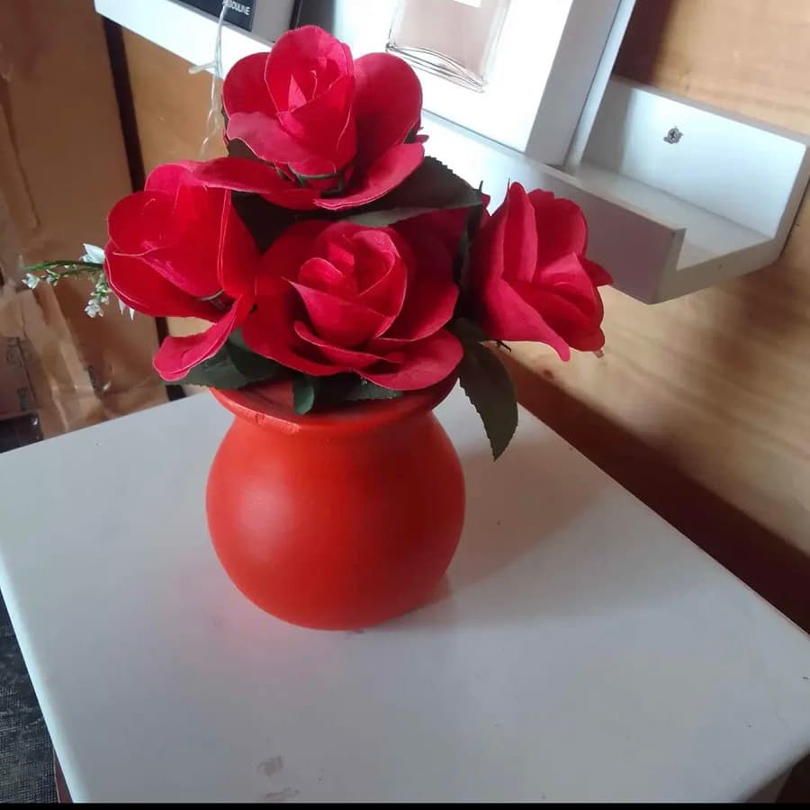 A round red vase holding roses, photographed on a white desk
