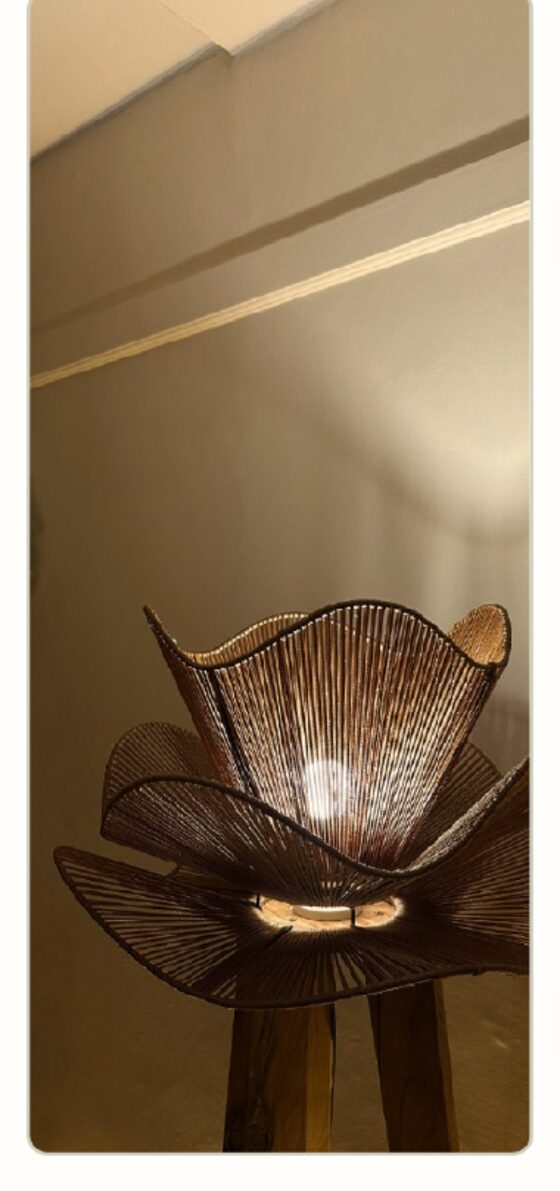 A woven petal floor lamp photographed on a phone against a plain Nairobi wall
